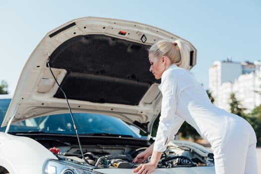 woman stands at the hood of a car repairing a car