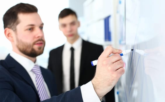Focus on male hand with marker. Manager writing in office and talking about business deal. Man in trendy suit and striped tie drawing chart. Company meeting concept. Blurred background