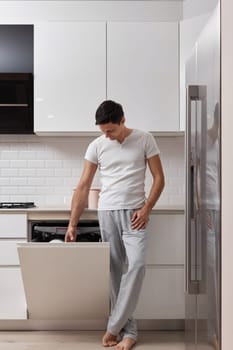 handsome husband man using dishwasher and washing dishes in white modern kitchen