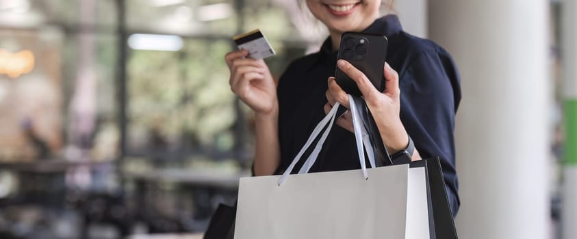 Portrait of attractive and playful Asian woman in casual clothes. Post a beautiful face showing off your credit card. View your collection on your mobile phone with Black Friday sales and discounts.