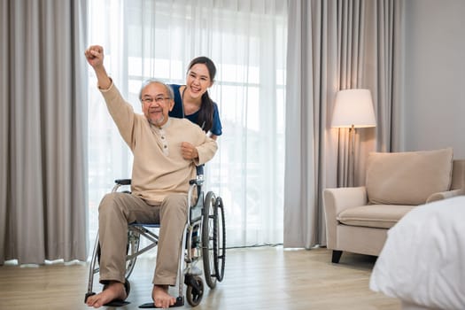 Happy curator person doctor pushing wheelchair and run elderly disabled patient freedom raising arm at hospital, senior retired man sitting on wheelchair having fun with young woman nurse, health care