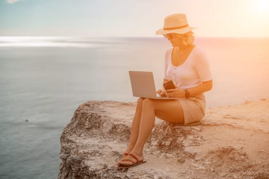 Freelance women sea working on the computer. Good looking middle aged woman typing on a laptop keyboard outdoors with a beautiful sea view. The concept of remote work