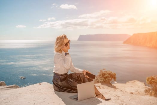 Business woman on nature in white shirt and black skirt. She works with an iPad in the open air with a beautiful view of the sea. The concept of remote work