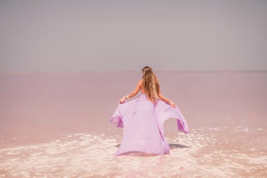 Woman pink salt lake. Against the backdrop of a pink salt lake, a woman in a long pink dress takes a leisurely stroll along the white, salty shore, capturing a wanderlust moment