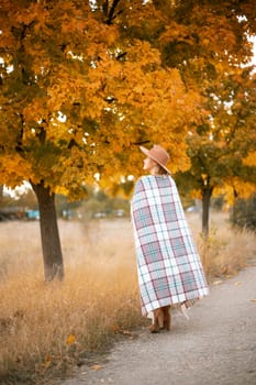 autumn woman in a brown hat, plaid, against the background of an autumn tree.