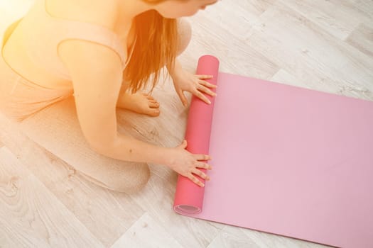 A young woman rolls a pink fitness or yoga mat before or after exercising, exercising at home in the living room or in a yoga studio. Healthy habits, keep fit, weight loss concept. Closeup photo.