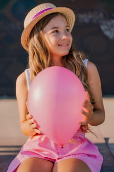 Portrait of a girl in a hat with a pink balloon. She is dressed in pink clothes and her hair is long and loose