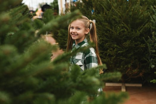 Small girl chooses a Christmas tree at the market.