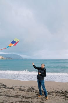 Young smiling man flying a colorful kite on a rope on the beach. High quality photo