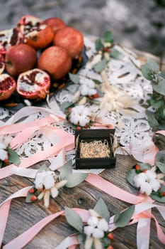 Wedding rings in a box lie on a wooden table on a macrame napkin among ribbons and fruits. High quality photo