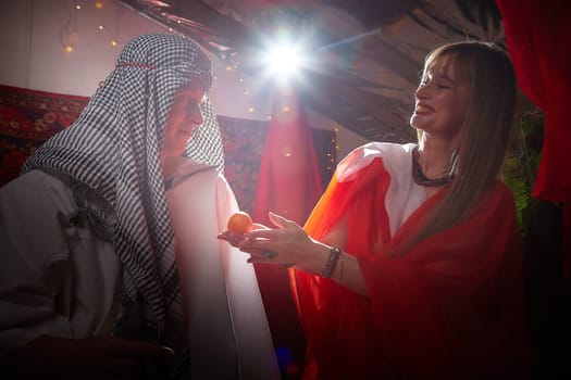 Portrait of young arabian muslim couple in traditional clothes in cozy red room. Fhoto shoot in easten style with male and female model like in harem with a sultan and an odalisque. Partial focus