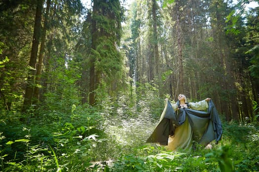 Adult mature woman 40-60 in a green long fairy dress in forest. Photo shoot in style of dryad and queen of nature. Fairy in beautiful green summer forest. Concept of caring for nature