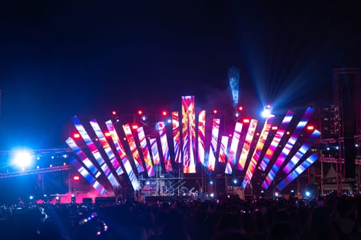 The night comes alive at a concert festival during the main event with a cheering crowd in front of the brightly lit stage. The lens flare captures the excitement and the fun of the music festival.