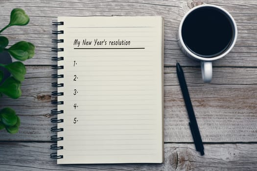 My new year's resolution text on notepad with pen, coffee and potted plant on wooden desk.