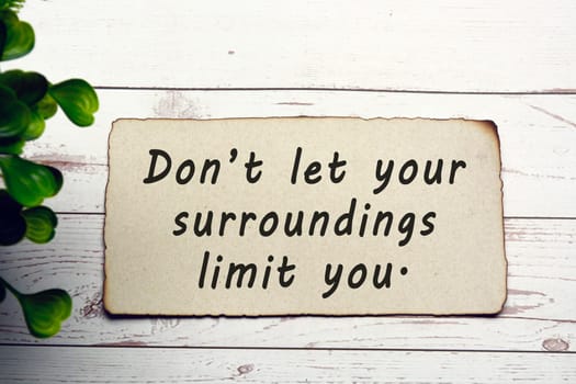 Motivational and inspirational quote on burnt edge brown paper on wooden desk - Dont let your surroundings limit you.
