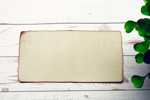 Burnt edge brown paper with space for text with blurred green plant on wooden desk. Copy space.