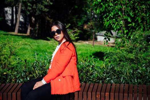 brunette woman rests on a bench by green plants