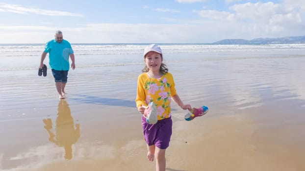 Little girl, braving the cold, joyfully runs in her swimsuit across the beach during winter.