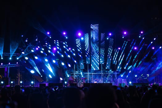 The night comes alive at a concert festival with a jubilant crowd in front of the brilliantly lit stage. The lens flare captures the excitement as unrecognizable people revel in joy of music event.