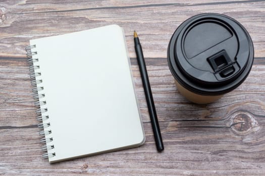 Directly above view of office desk with pen, notepad and disposable coffee cup. Flat lay. Copy space.