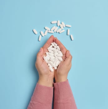 Two female hands hold white oval pills on a blue background, top view