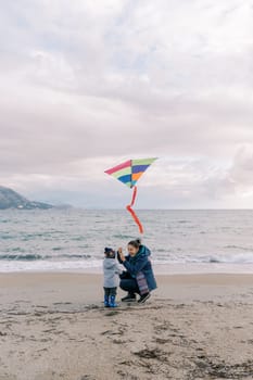 Happy mom crouched next to a little girl with a colorful kite near the sea. High quality photo