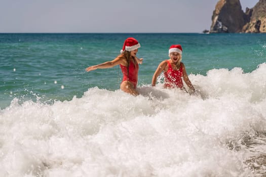 Women in Santa Claus hats run into the sea dressed in red swimsuits. Celebrating the New Year in a hot country.