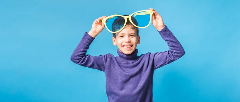 Cheerful little boy generation alpha in big glasses express a surprised face holds mockup board isolated on blue background with copy space.