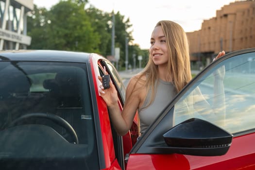 Beautiful young woman with long hair standing near new red car.