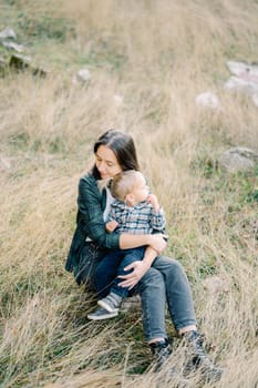 Mom hugs a little girl in her arms with closed eyes sitting on the lawn. High quality photo