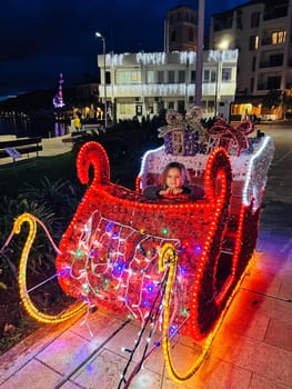 Little girl sits in Santa sleigh glowing with lights. High quality photo