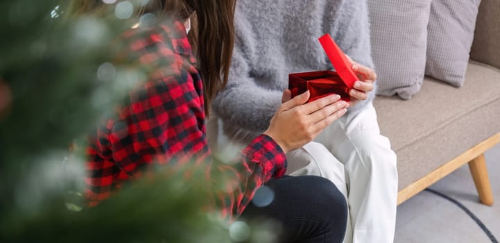 Cute young woman holds a gift box to surprise his mother on Christmas Day. 60 year old retired woman happy Happy daughter on Christmas day in living room holding red gift box.