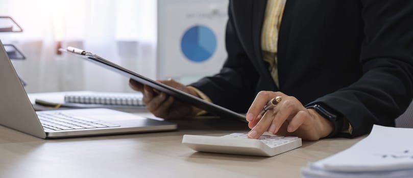 Close up, Businesswoman uses calculator to calculate finances, mathematics on table in office and business charts, tax, accounting, statistics and analytical research concept..