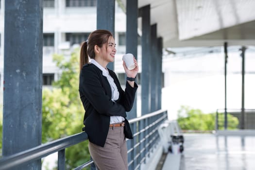 Portrait of a confident Asian businesswoman standing with a coffee cup on a skywalk in the morning. smiling and be happy to start work..