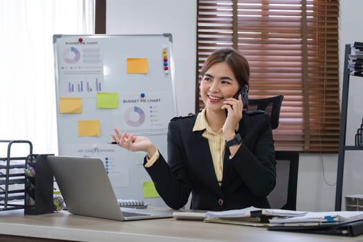 Businesswoman using laptop to do finance, talking on phone, working with numbers on wooden table in office and business background, tax, accounting, statistics and analytical research concept..