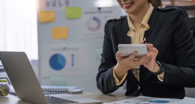 Close up Business woman using calculator and laptop for do math finance on wooden desk in office and business working background, tax, accounting, statistics and analytic research concept.