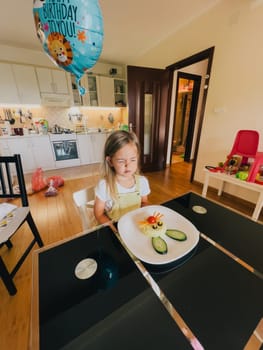 Little birthday girl sits in front of a plate of rabbit-shaped rice at the table. High quality photo