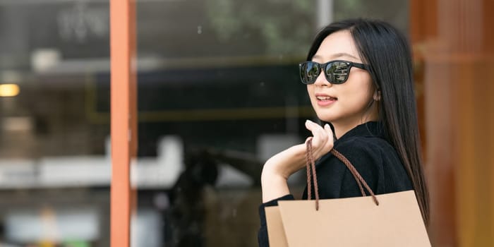 Young asian woman in shopping. Fashion woman in black with shopping bag walking around the city after shopping. Black friday.