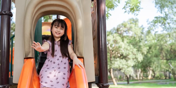 Happy children girl sliding and playing at outside playground in the park on summer vacation, outdoor activity at school or playground.