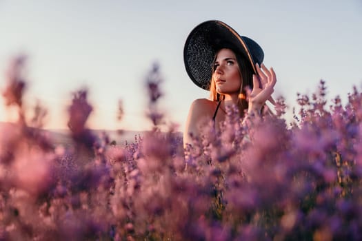 Close up portrait of young beautiful woman in a white dress and a hat is walking in the lavender field and smelling lavender bouquet.