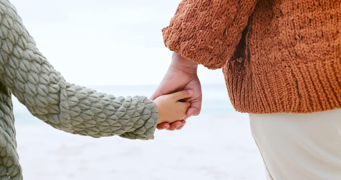 Parent, child and holding hands at ocean for love, care or support in trust, travel or outdoor getaway. Closeup of person with kid for unity, bonding or compassion on beach or sea coast together.