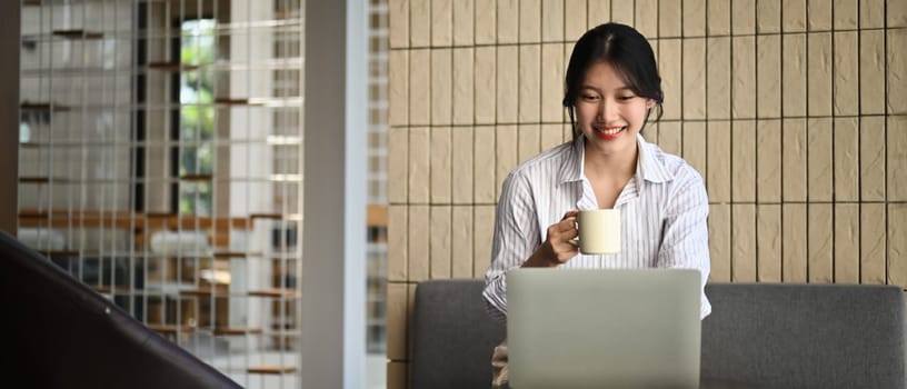 Attractive businesswoman drinking coffee and using laptop in office lounge.