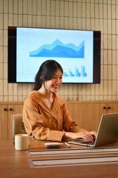 Charming Asian businesswoman sitting in meeting room and working on laptop computer.