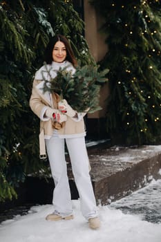 A girl with long hair in winter on the street with a bouquet of fresh fir branches.