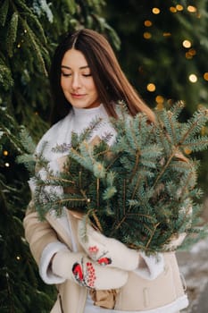 A girl with long hair in winter on the street with a bouquet of fresh fir branches.