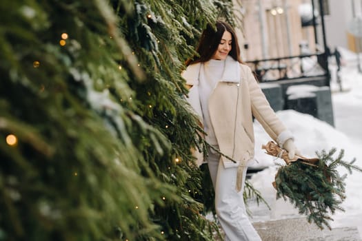 A girl with long hair in winter on the street with a bouquet of fresh fir branches.