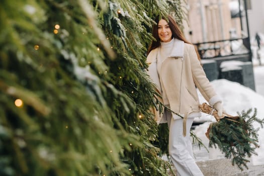 A girl with long hair in winter on the street with a bouquet of fresh fir branches.