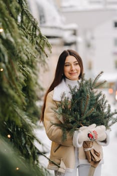 A girl with long hair in winter on the street with a bouquet of fresh fir branches.