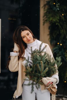 A girl with long hair in winter on the street with a bouquet of fresh fir branches.