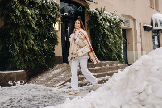 A girl with long hair in a scarf and with a white handbag walks down the street in winter.